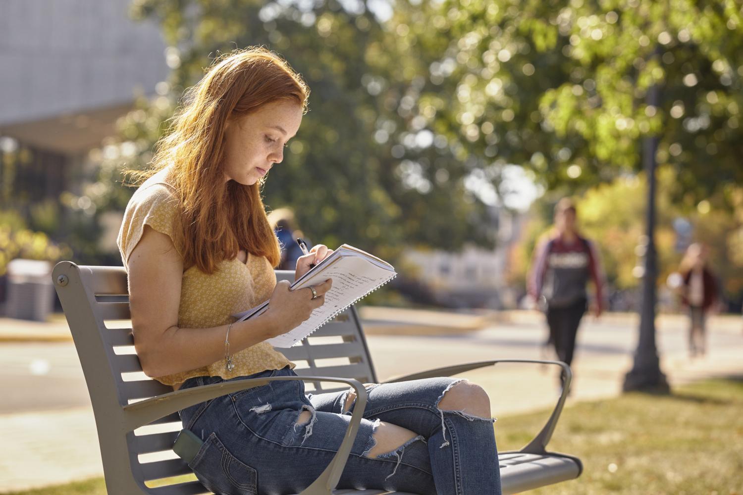 A <a href='http://l7cm.vijethaschool.com'>BETVLCTOR伟德登录</a> student reads on a bench along Campus Drive.